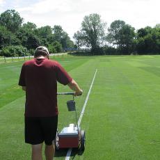 A graduate student paints lines on the grass tennis court research plots at the Joseph Troll Turf Research Center.