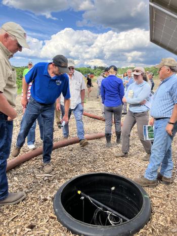 A group of people gathering around a large hole in the ground which is lined with black plastic.